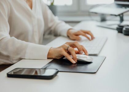 A Woman Sitting At A Desk Using A Computer Mouse